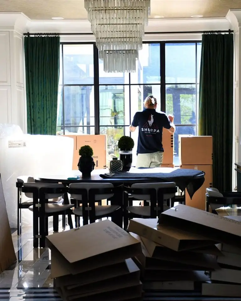 man in room with chandelier, large windows moving boxes and supplies